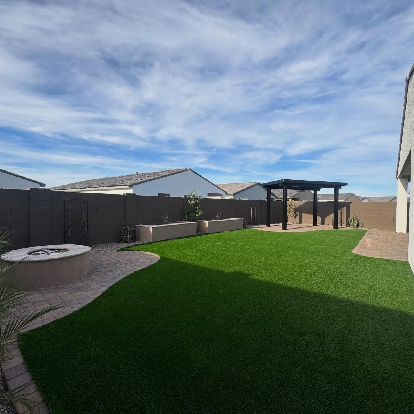 Complete backyard remodel with curved artificial turf, a paver patio and round fire pit, raised planters and a black aluminum pergola