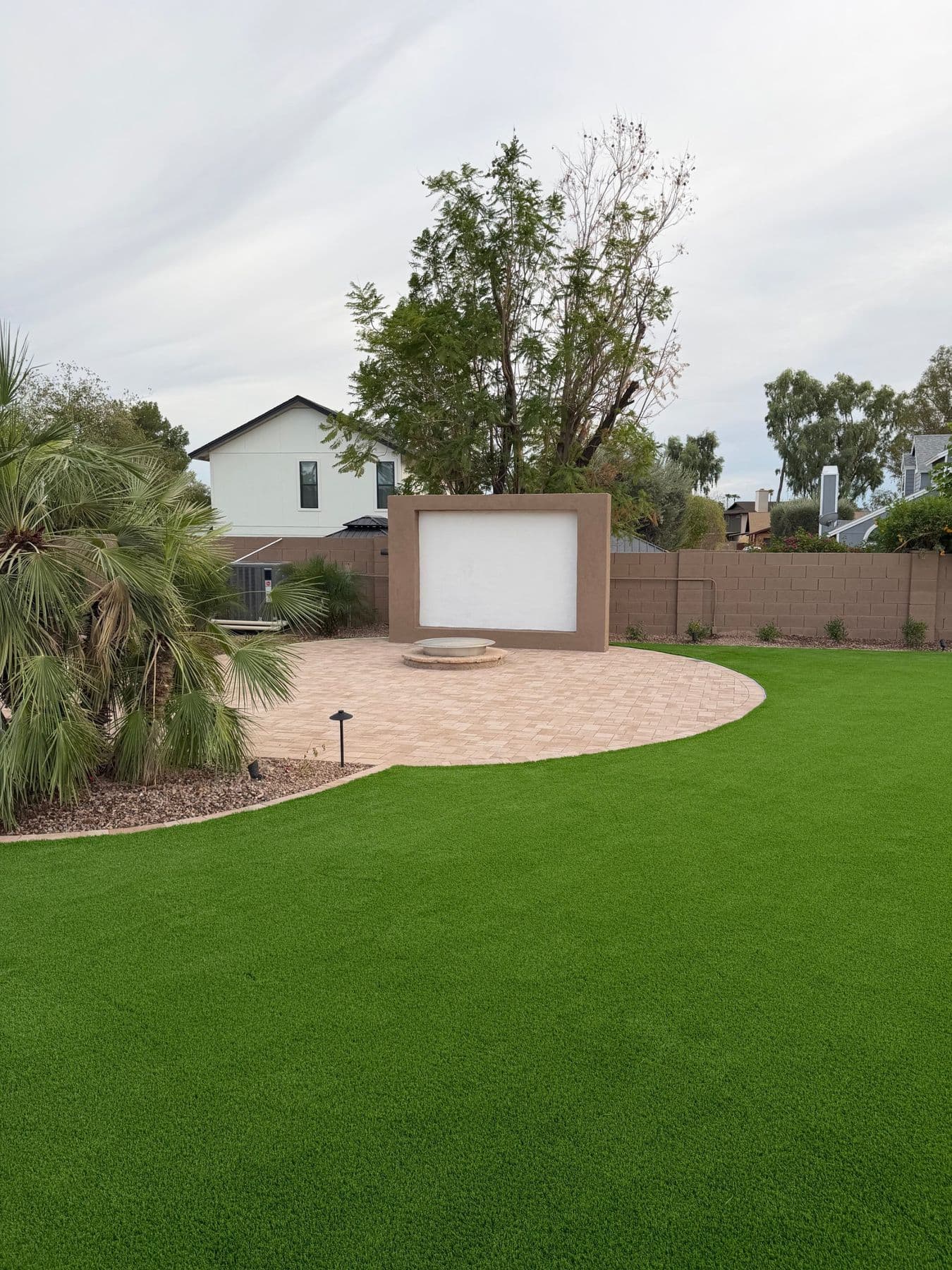 Circular paver patio with a fire pit and feature wall, surrounded by turf