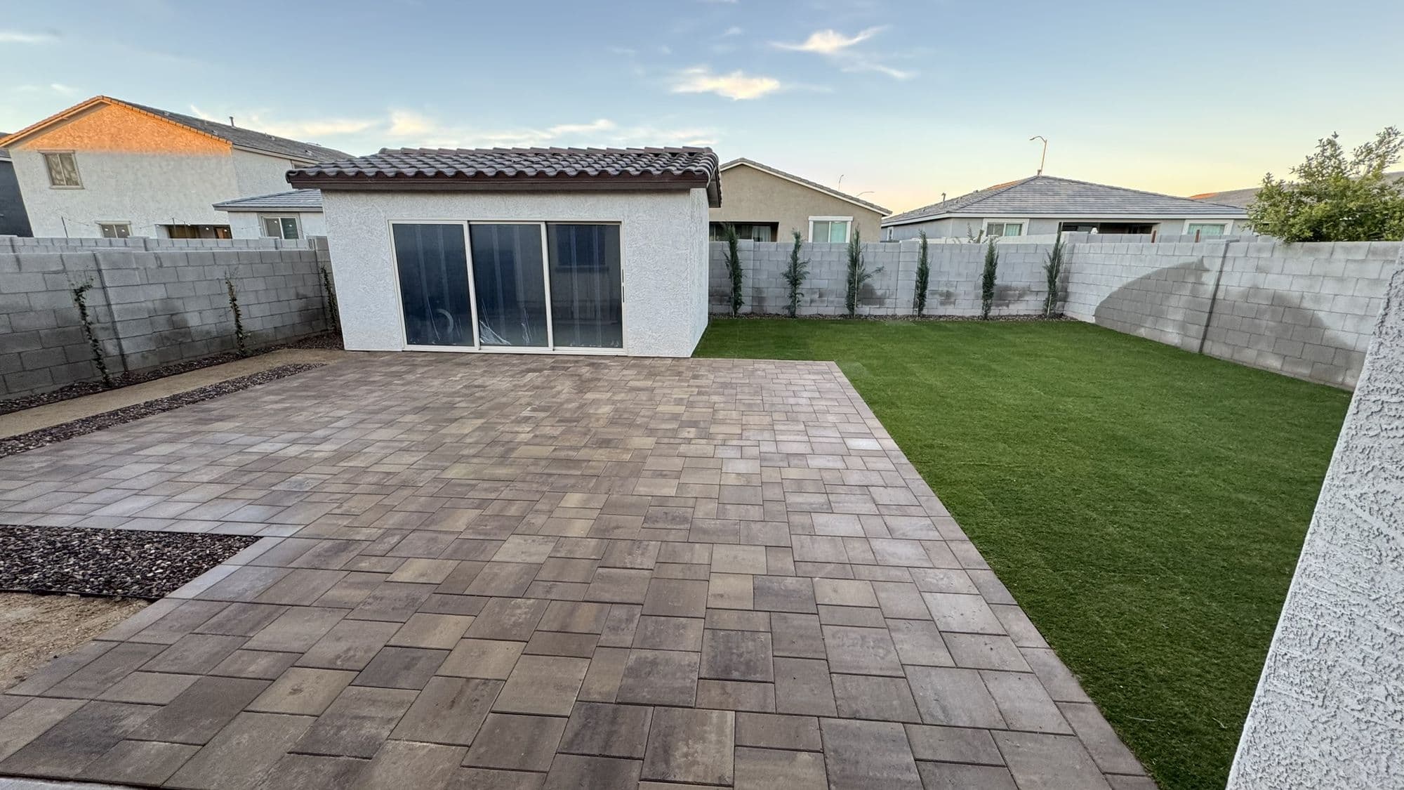 Belgard Dimensions 12 paver patio beside a Tahoma 31 grass lawn with Arizona cypress along the wall