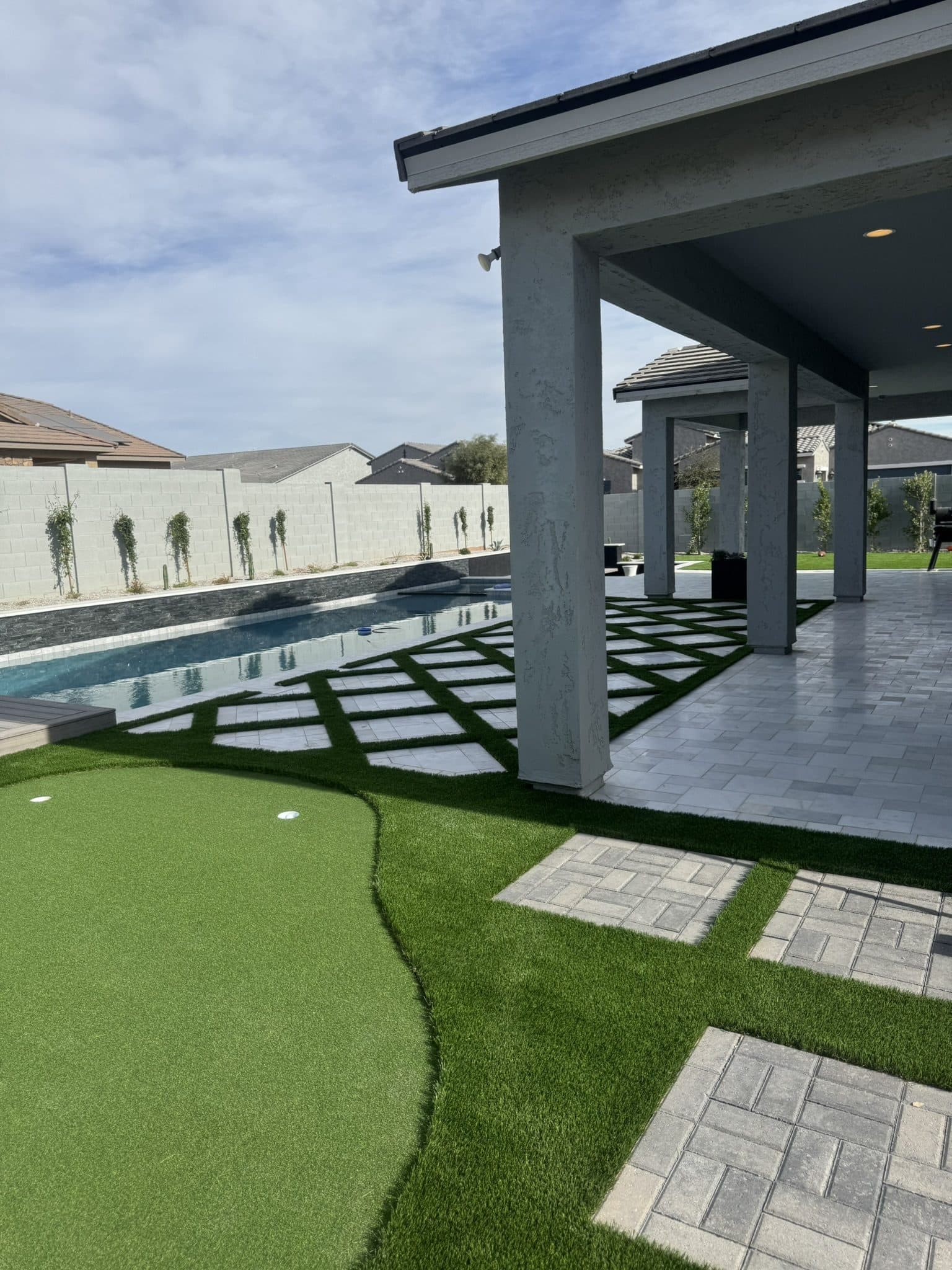 Putting green beside a pool deck of gray marble pavers set in turf