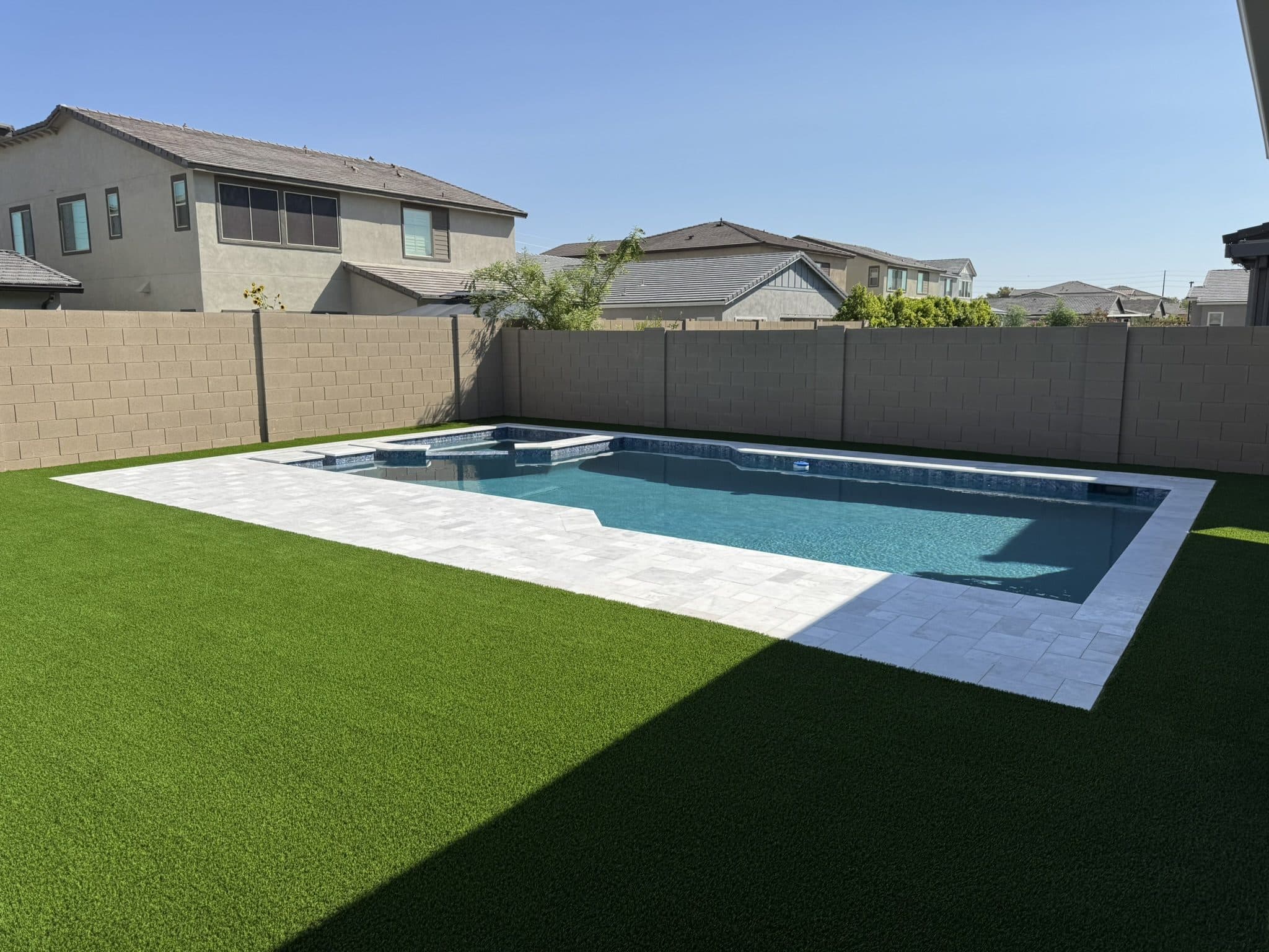 Pool deck of marble travertine pavers surrounded by artificial turf