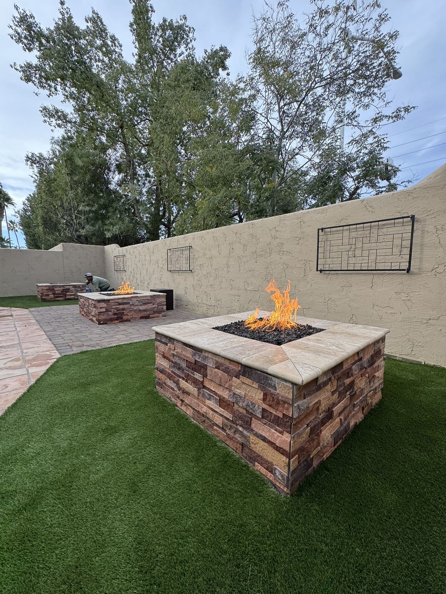 Three square propane fire pits with natural stone veneer and travertine caps along a stucco wall