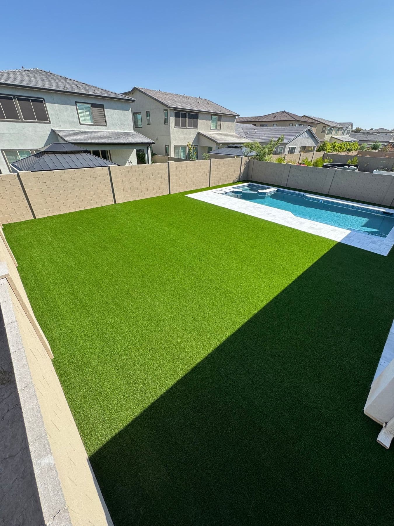 Large artificial turf lawn beside a swimming pool with light paver decking