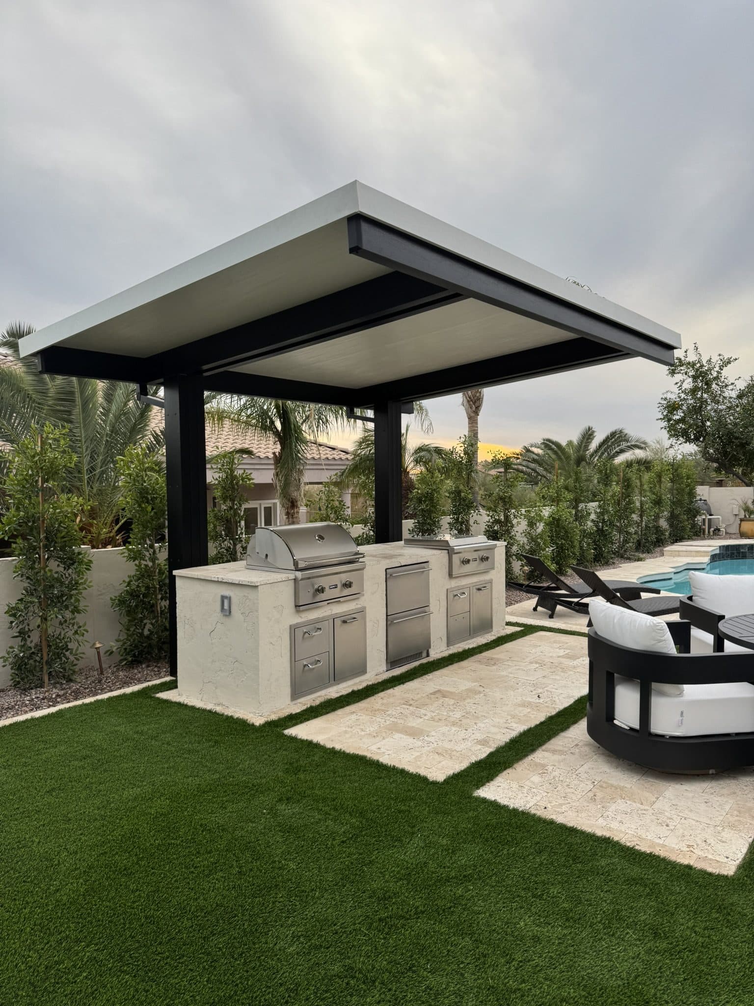 Custom outdoor kitchen with a grill under a cantilever pergola on ivory travertine