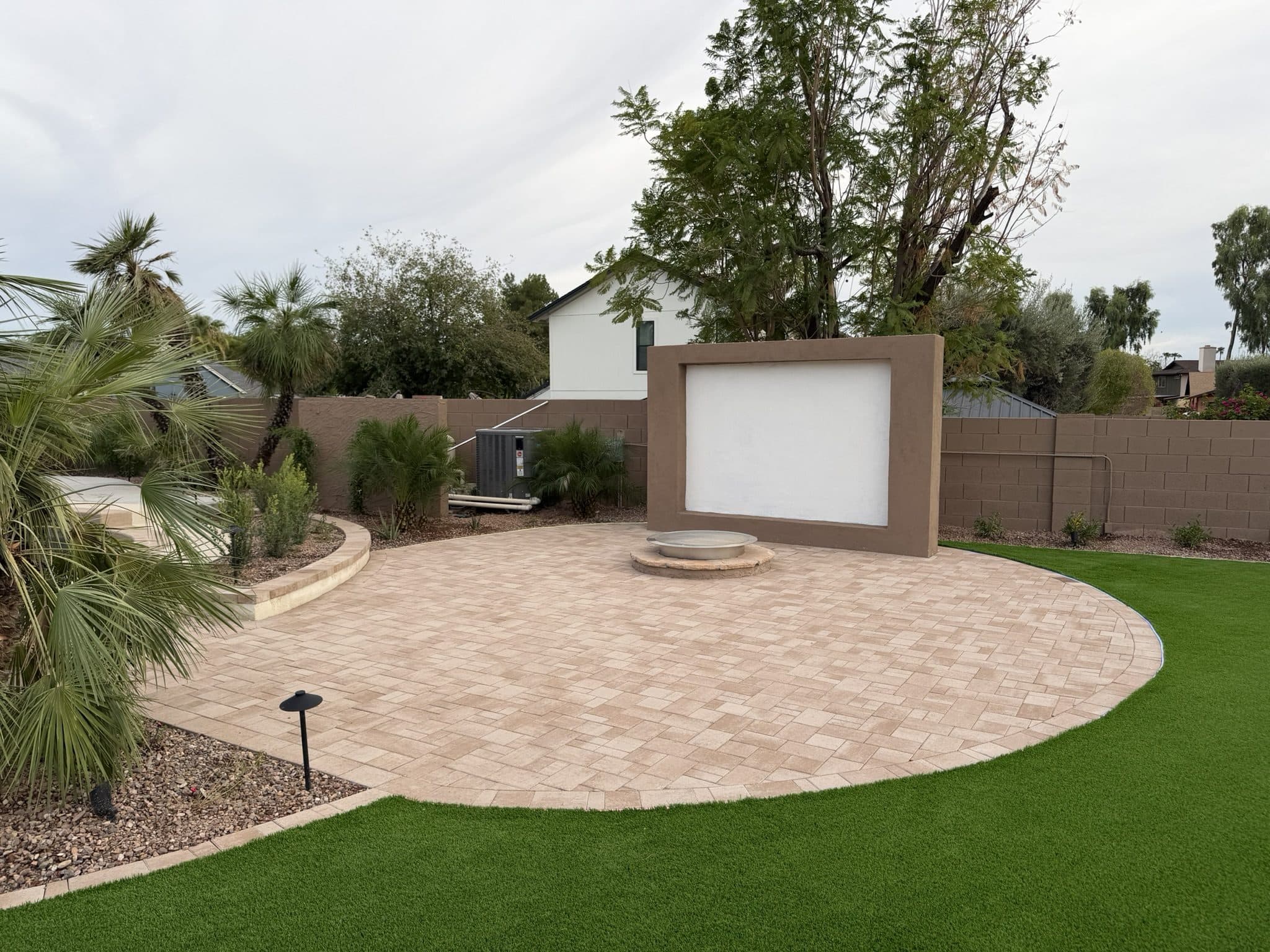 Circular Belgard paver patio in front of a media wall, surrounded by turf