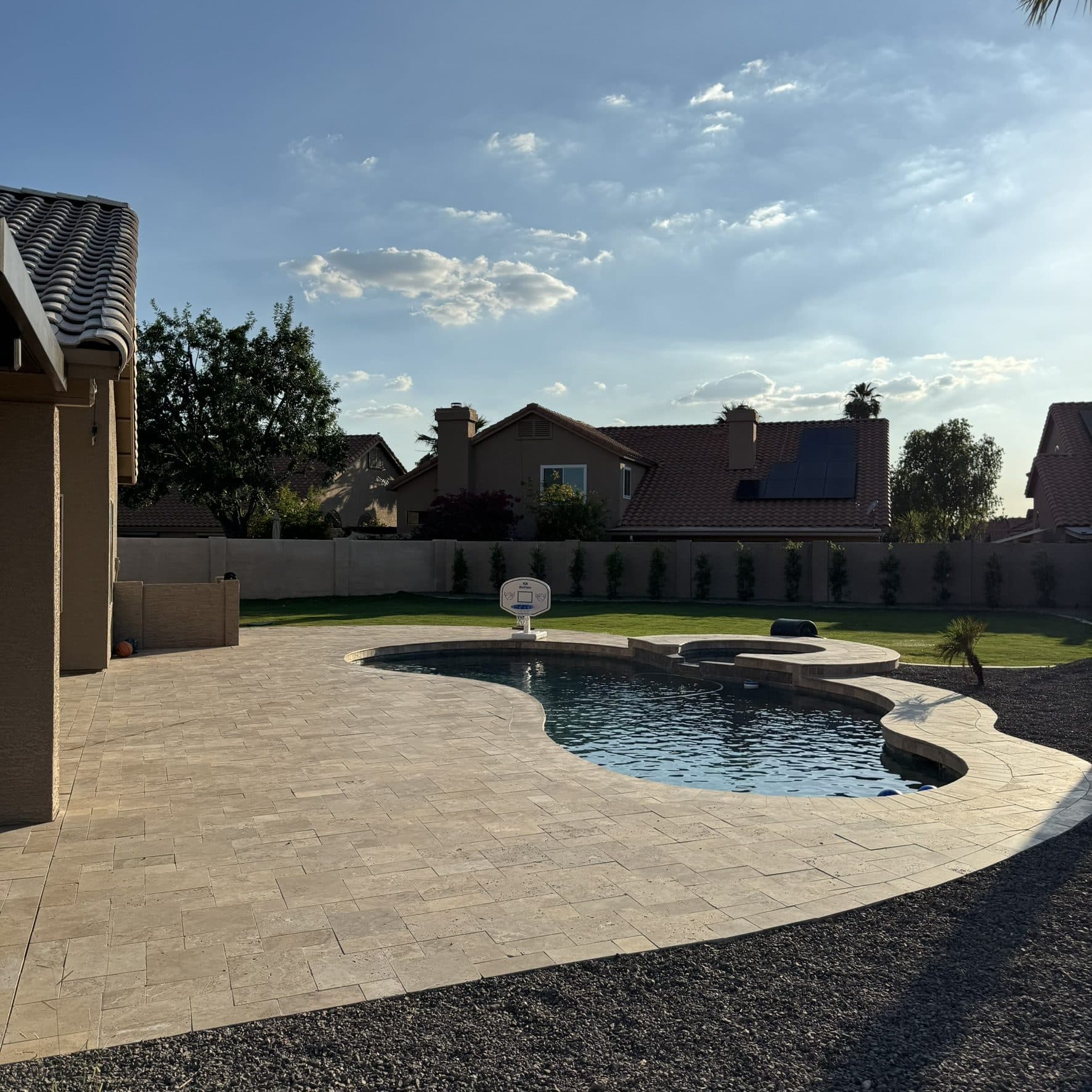 Dark walnut travertine pool deck with turf and a sod lawn beyond