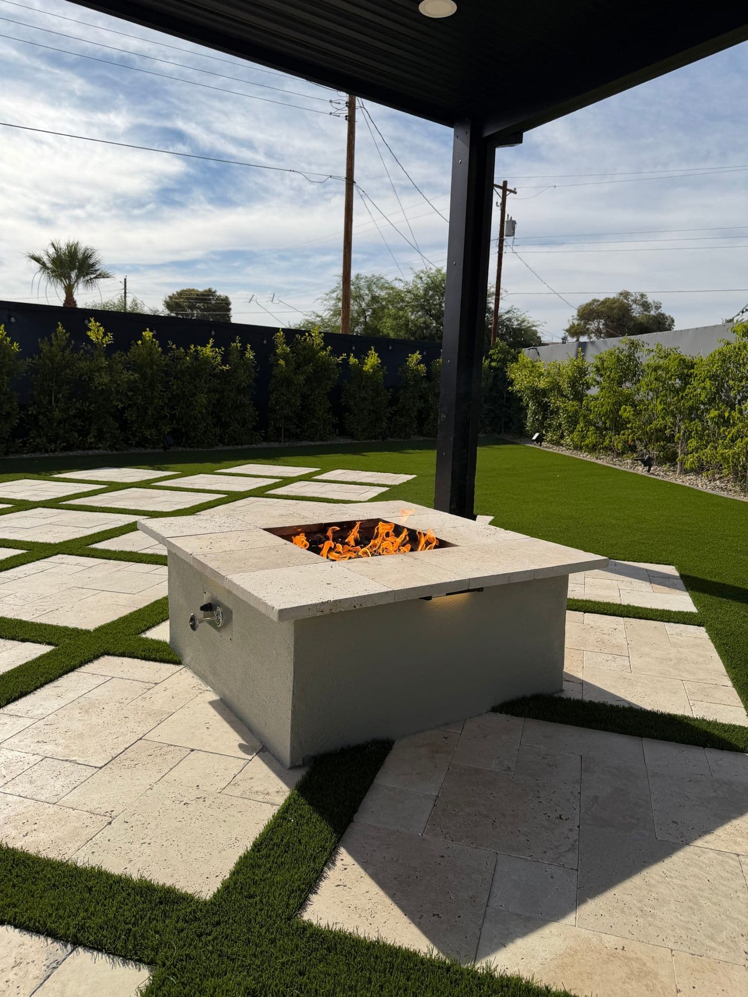 Propane fire pit with a travertine cap on ivory travertine pads under a pergola