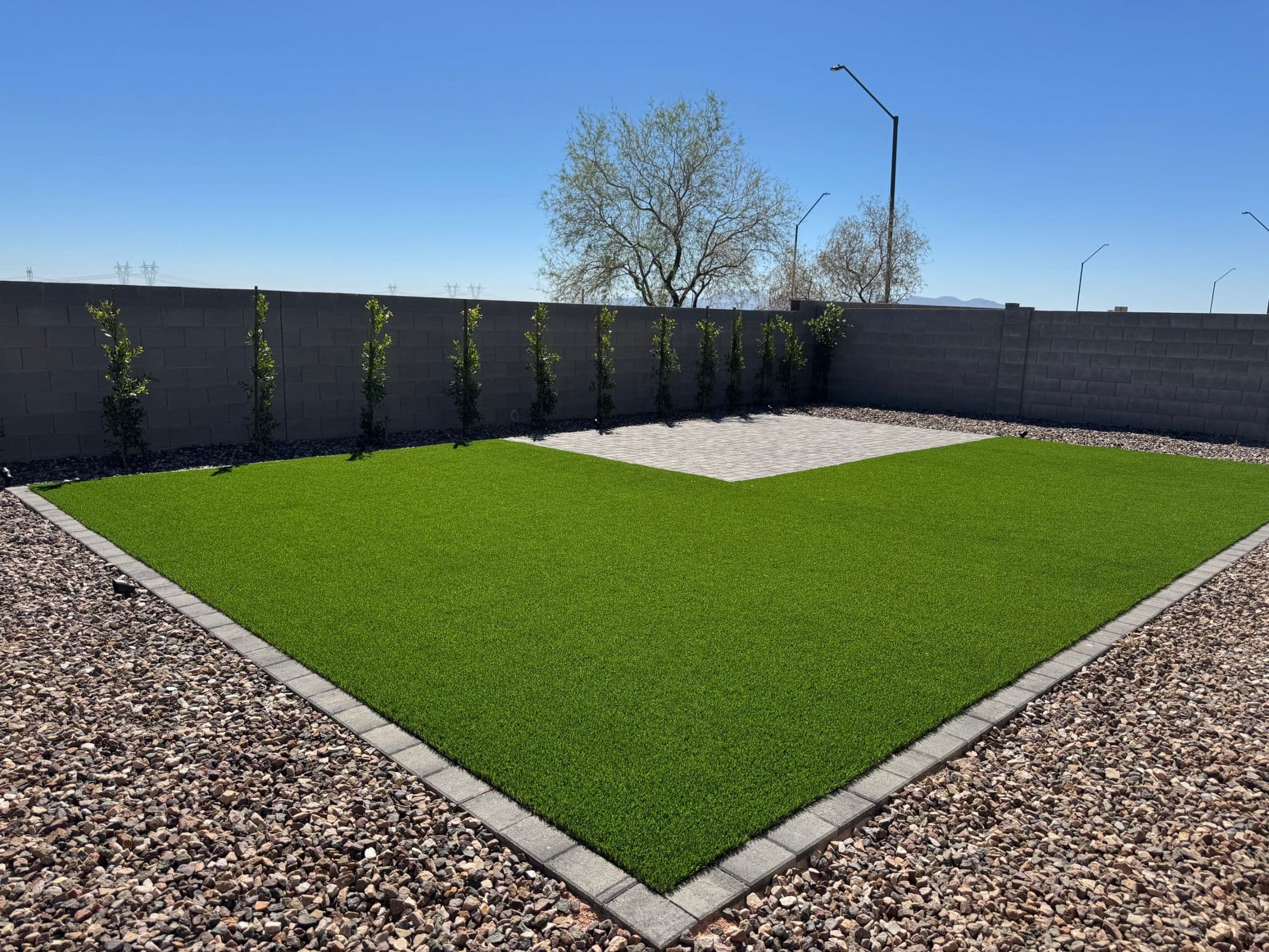 Artificial turf lawn with a paver border, paver patio, decorative rock and new trees