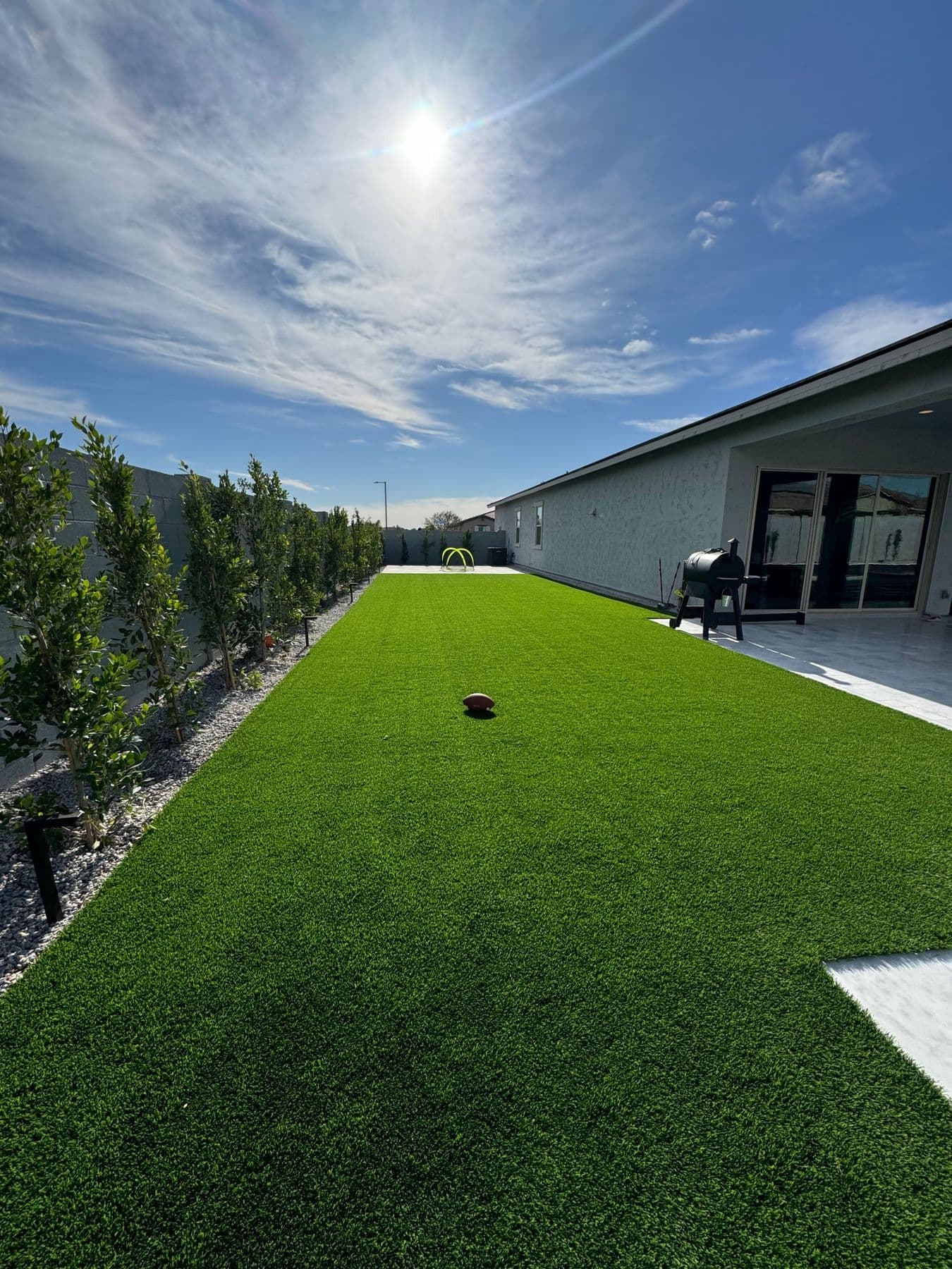 Artificial turf lawn edged with rock and a row of privacy trees